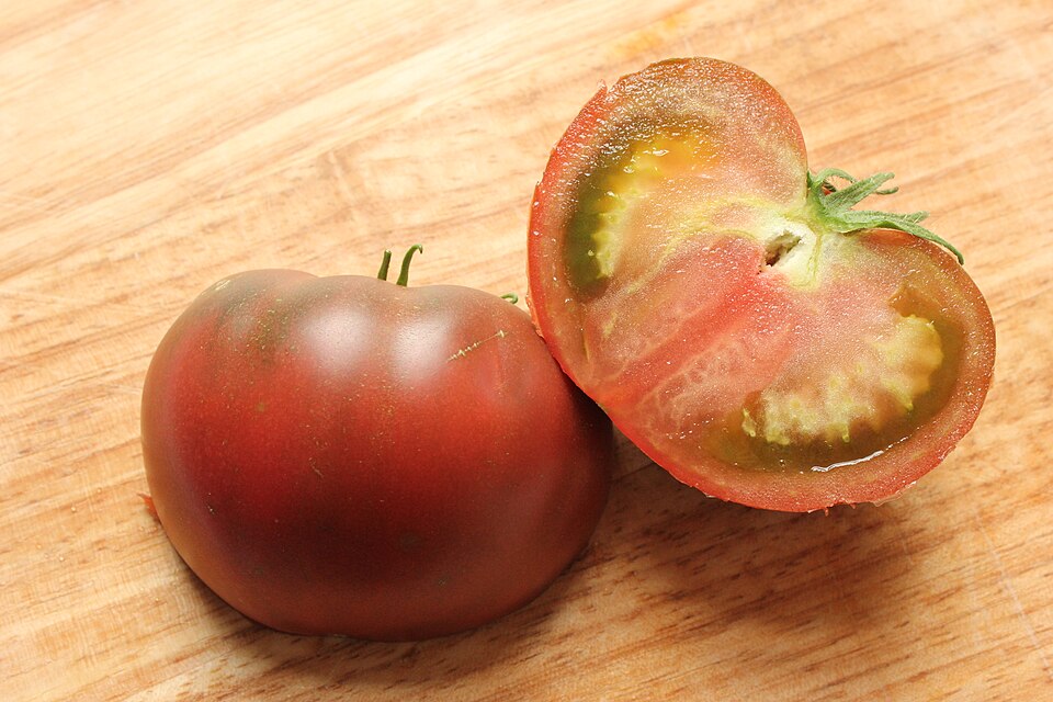 Cut Black Krim tomato beside a whole fruit, showing the interior and dark shoulders.