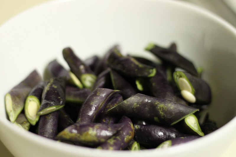 Cut purple Royal Burgundy bean pods in a white bowl, shown as a culinary reference.